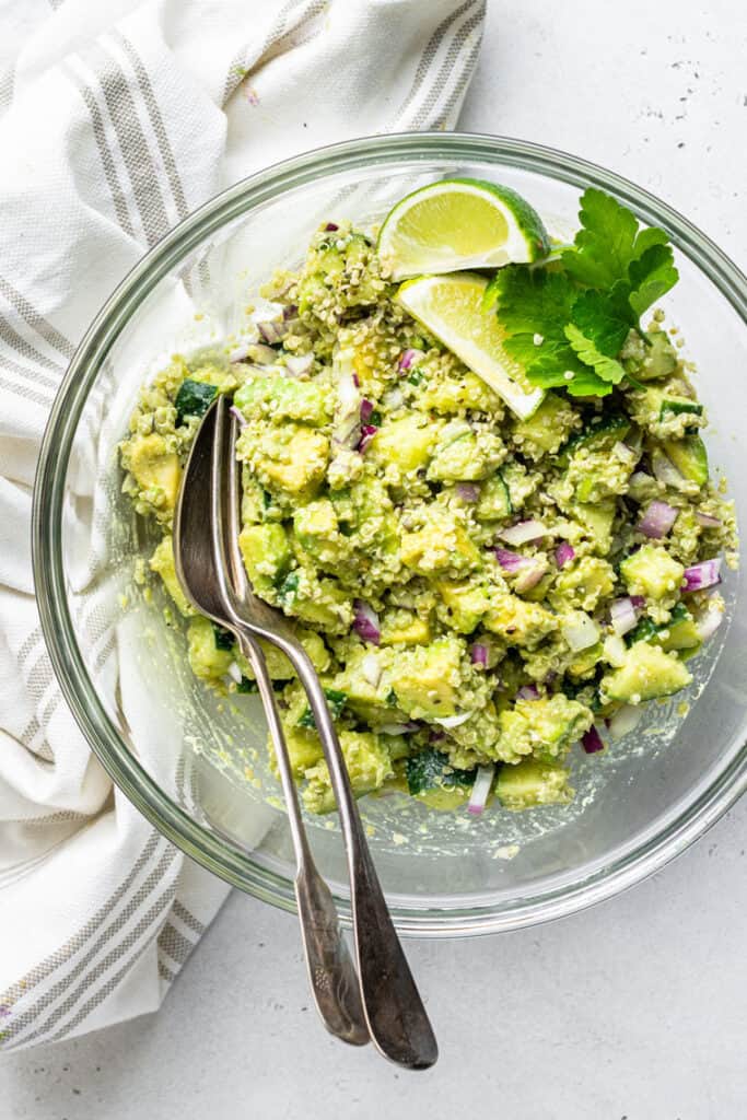 The best cucumber quinoa salad recipe with avocado and creamy cashew herb dressing. It makes a delicious and light vegan lunch or dinner! large glass bowl with cucumber quinoa salad with lime and cilantro