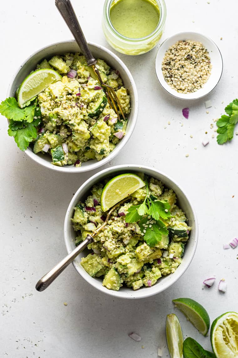 two white bowls with cucumber avocado quinoa salad with lime and cilantro