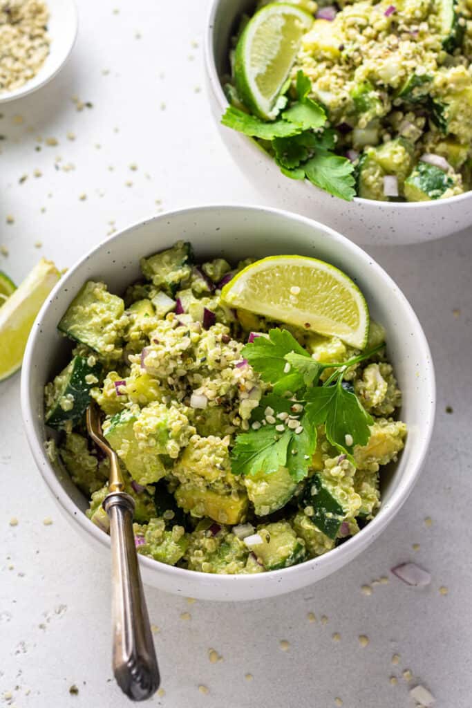 The best cucumber quinoa salad recipe with avocado and creamy cashew herb dressing. It makes a delicious and light vegan lunch or dinner! white bowl with cucumber quinoa salad with lime and cilantro