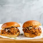 Side view of two vegan lentil sloppy joe sandwiches on a wooden cutting board with parchment paper