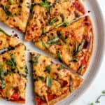 overhead of a plate with six slices of pizza made with quinoa crust and melted cheese with tomato sauce topped with fresh basil and red pepper flakes