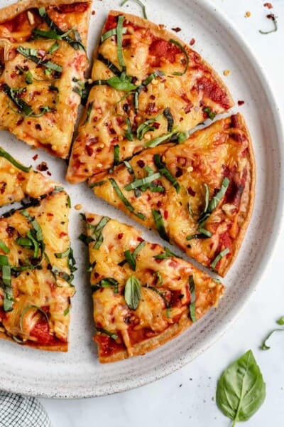 overhead of a plate with six slices of pizza made with quinoa crust and melted cheese with tomato sauce topped with fresh basil and red pepper flakes