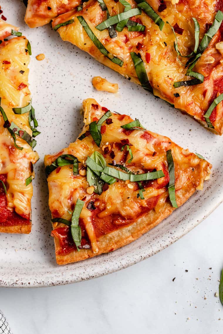 close up overhead of a slice of pizza made with quinoa crust and vegan cheese with a bite taken out on a white speckled dinner plate