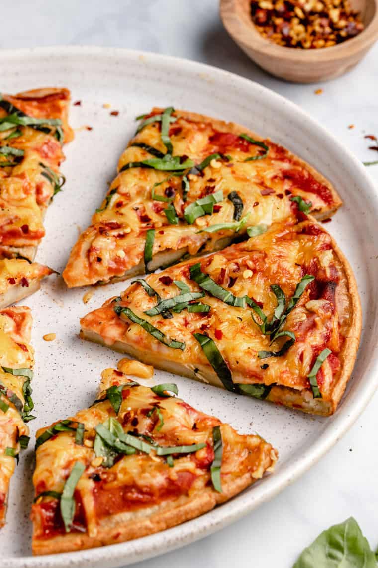 45 degree shot of slices of quinoa pizza crust with melted cheese, tomato sauce and fresh basil on a white speckled dinner plate