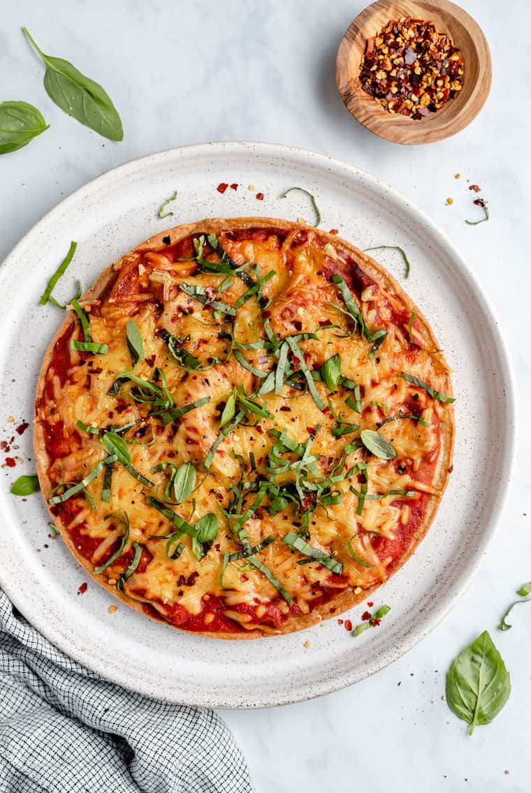 overhead of a whole pizza made with quinoa crust topped with tomato sauce, cheese and fresh herbs