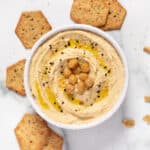 vegan hummus in white speckled bowl with crackers and garnishes