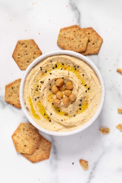 vegan hummus in white speckled bowl with crackers and garnishes