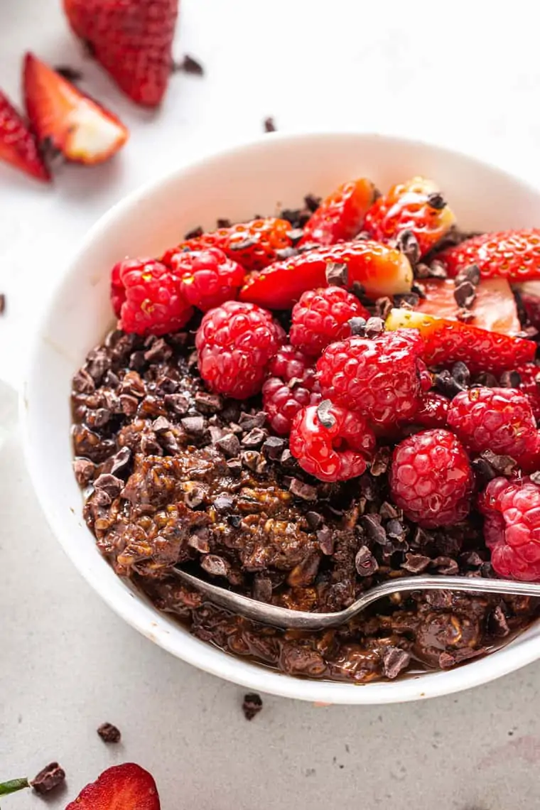 close up on a white bowl with chocolate protein oatmeal topped with fresh red berries