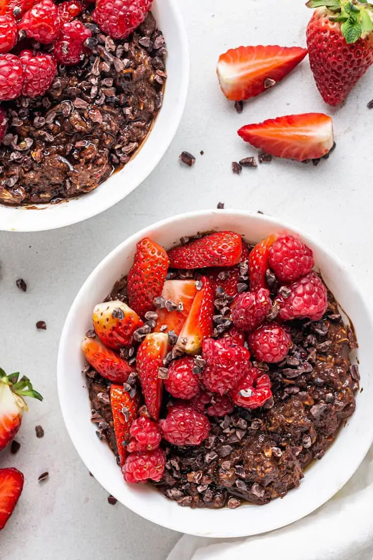 overhead of a white bowl with chocolate oatmeal topped with strawberries and raspberries