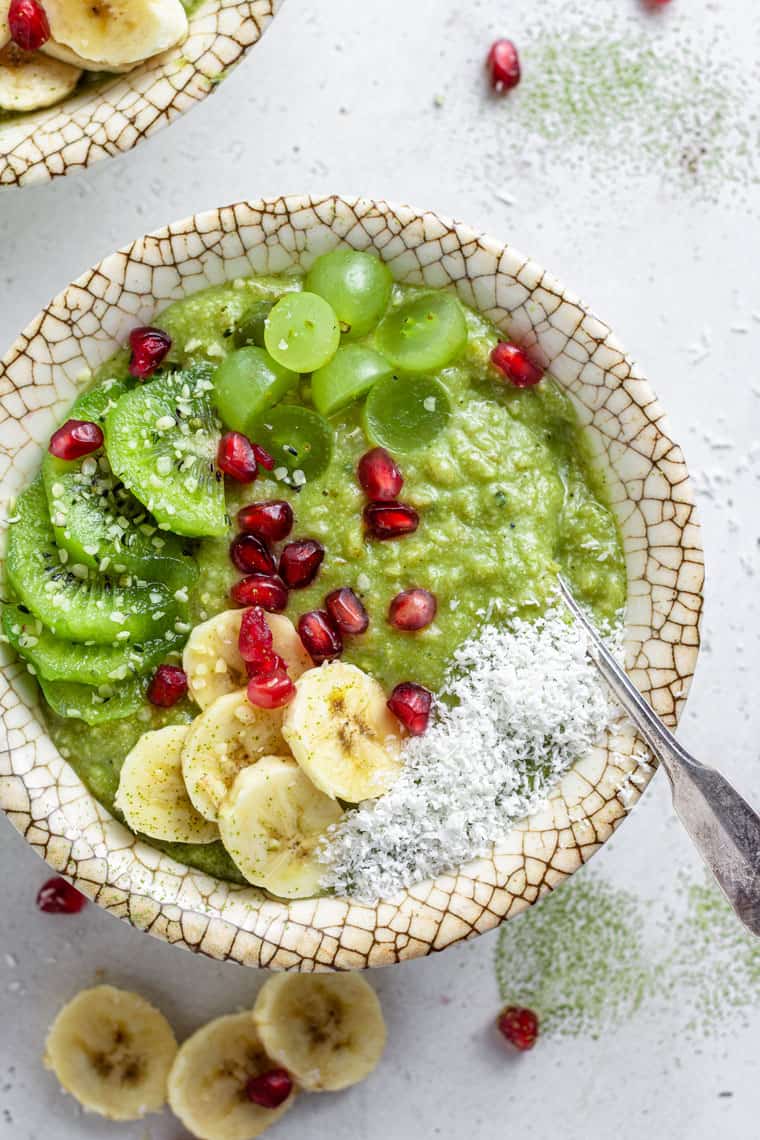 overhead of a bowl with green coconut matcha oatmeal topped with kiwis, grapes, bananas and pomegranate seeds