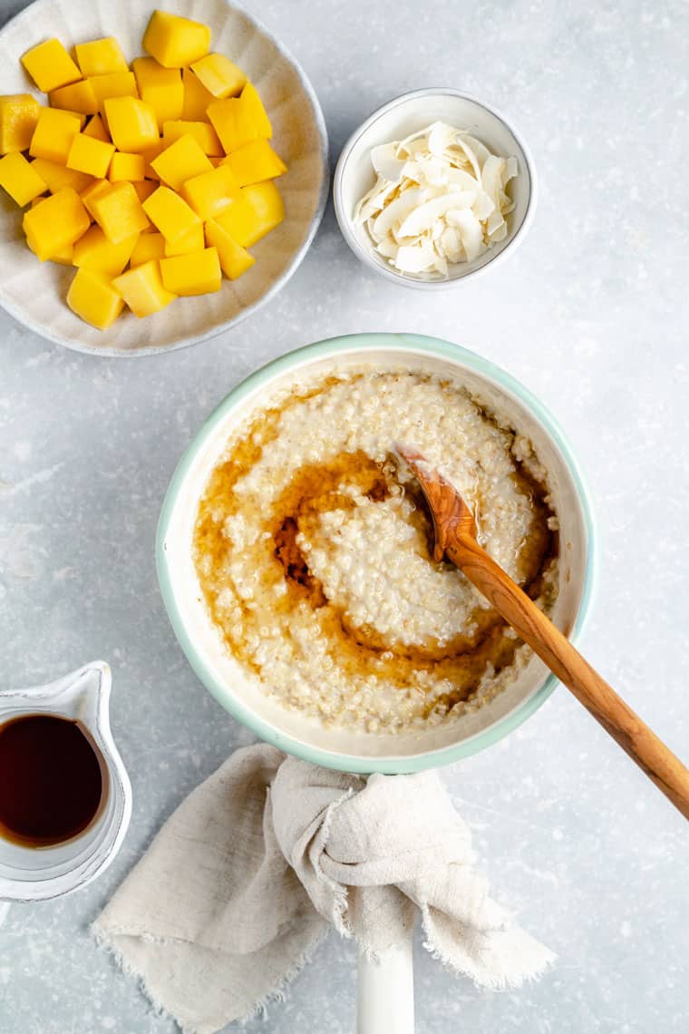 overhead of a pot with steel cut oats stirring maple syrup in with a bowl of mango on the side