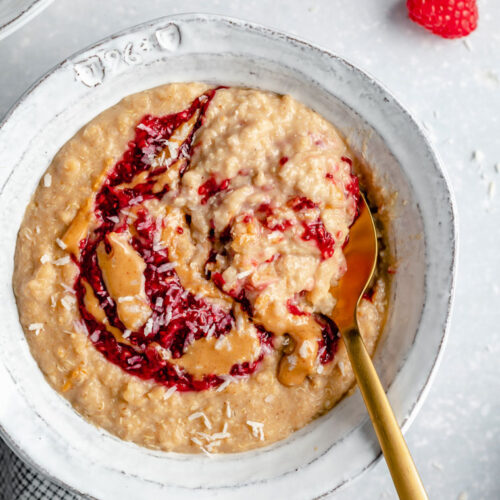 overhead of a bowl of creamy oatmeal with peanut butter, jelly and coconut on top