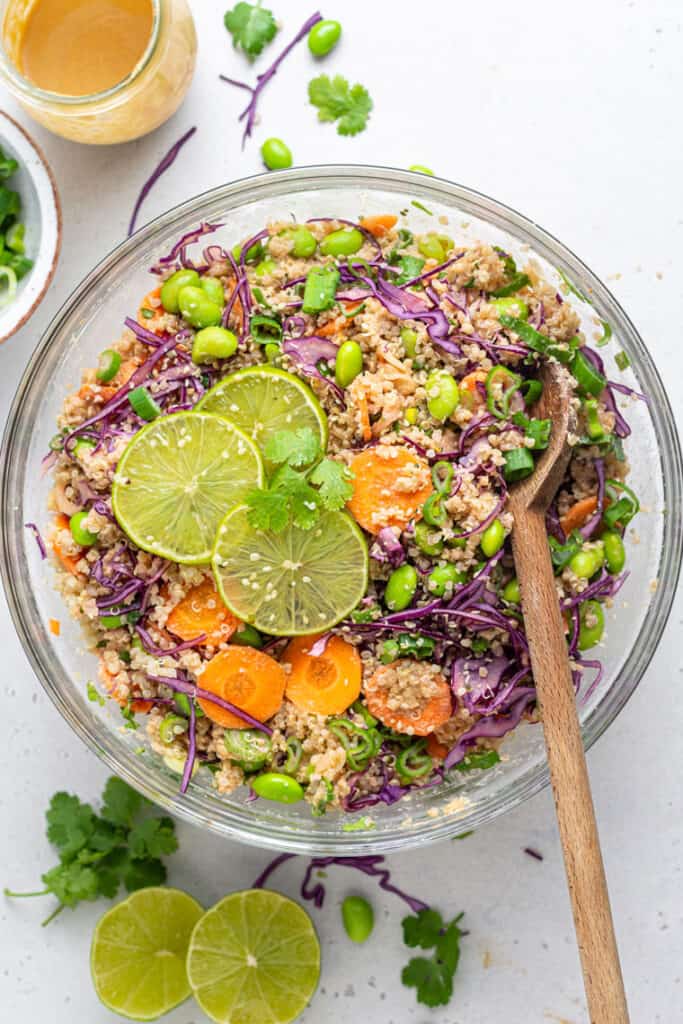 Overhead view of an Asian quinoa salad tossed with miso dressing in a glass bowl with a wooden spoon.