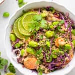 overhead of a white bowl with asian salad of quinoa, carrots, edamame, purple cabbage and lime