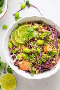 overhead of a white bowl with asian salad of quinoa, carrots, edamame, purple cabbage and lime