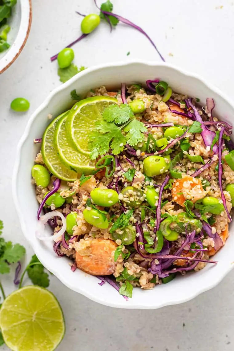 overhead of a white bowl with asian salad of quinoa, carrots, edamame, purple cabbage and lime