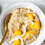 close up on a bowl of steel cut oats with coconut chips and mango cubes