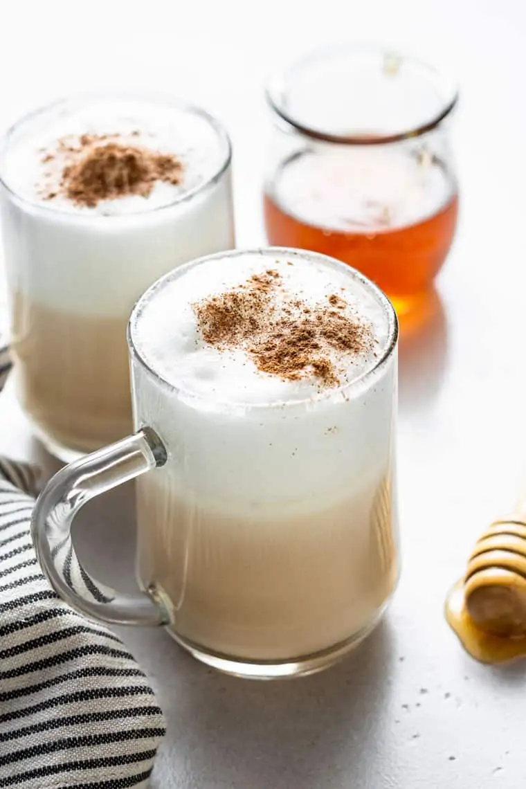 Side view of two glass mugs of london fogs with cinnamon on top.