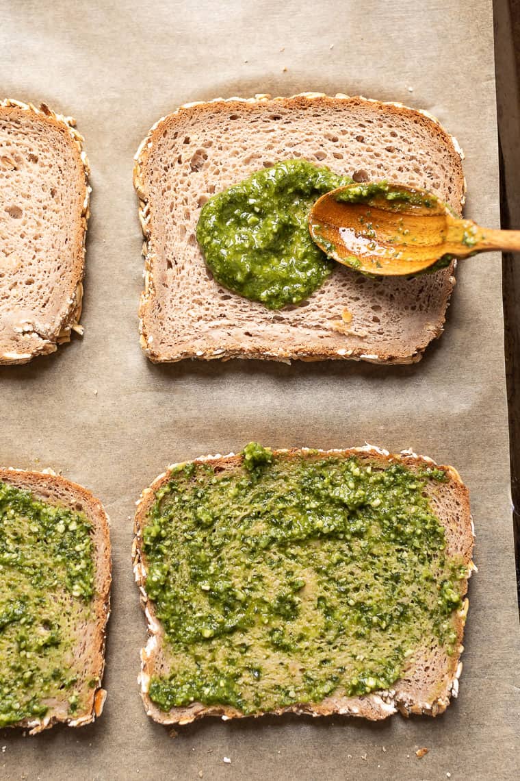 overhead of four slices of whole wheat bread with green pesto spread on top