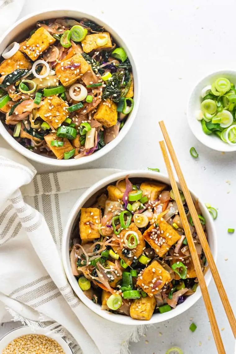 overhead of two white bowls with tofu egg roll stir fries with wooden chopsticks