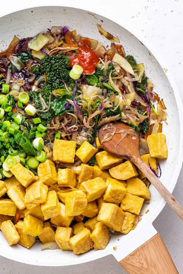 overhead of a white frying pan with ingredients for tofu egg roll bowls and a wooden spoon