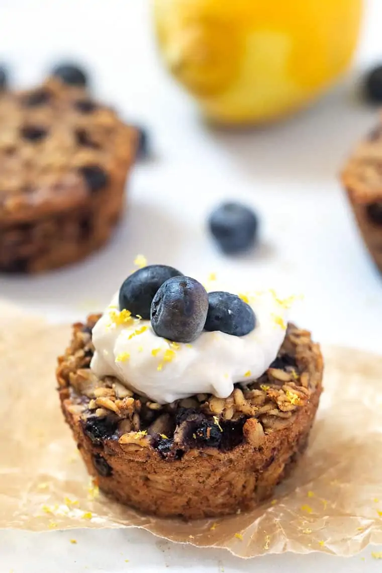 close up baked oatmeal cups with blueberries and lemon zest topped with yogurt and fresh blueberries