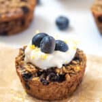 close up baked oatmeal cups with blueberries and lemon zest and topped with yogurt and blueberries