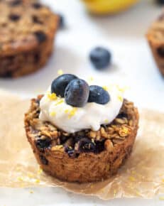 close up baked oatmeal cups with blueberries and lemon zest and topped with yogurt and blueberries