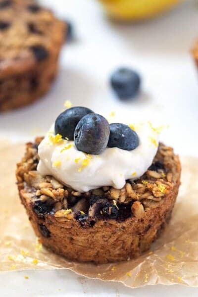 close up baked oatmeal cups with blueberries and lemon zest and topped with yogurt and blueberries
