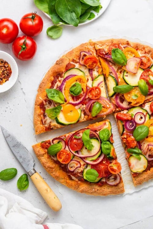 overhead of gluten free vegetable pizza with fresh herbs and tomatoes cut into four slices