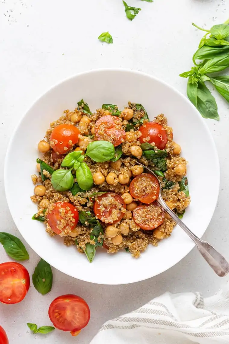 overhead of a white bowl with fresh tomato and basil quinoa salad
