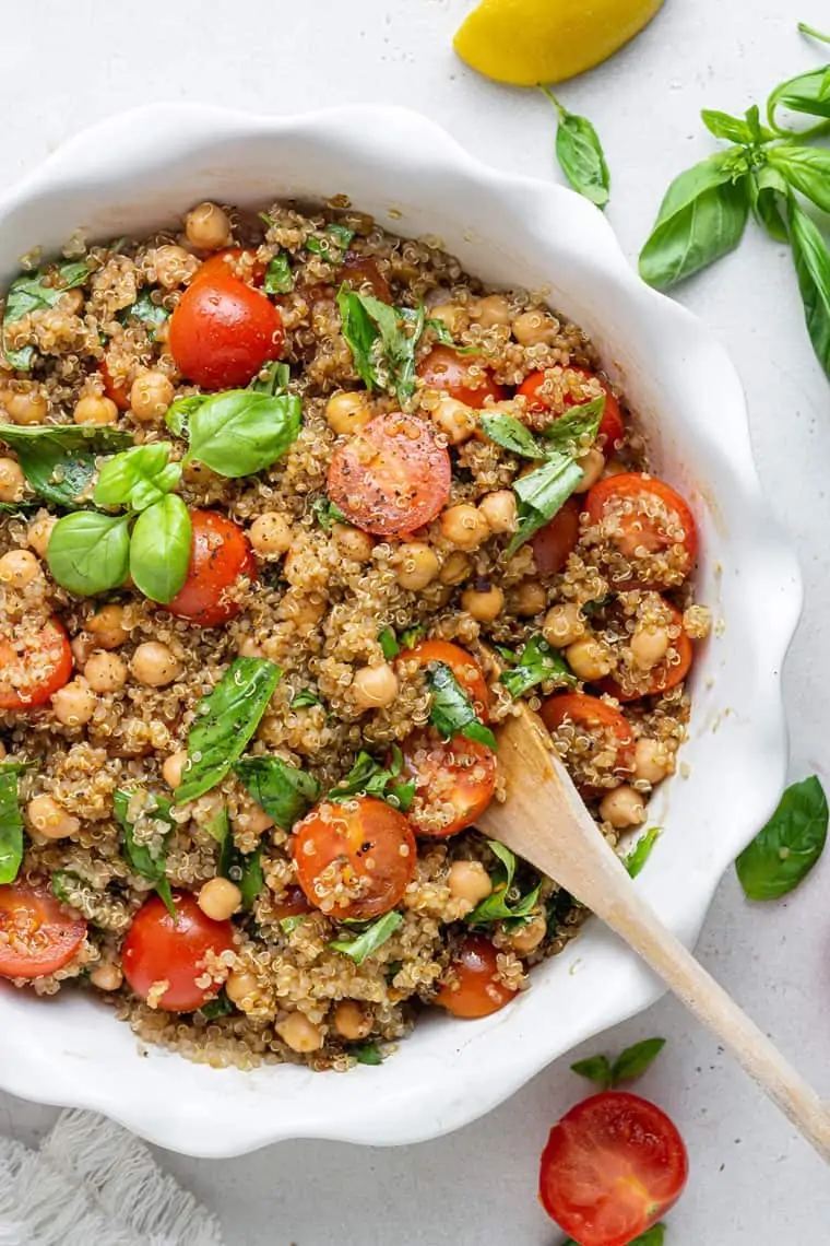 overhead of white bowl with quinoa caprese salad and fresh basil