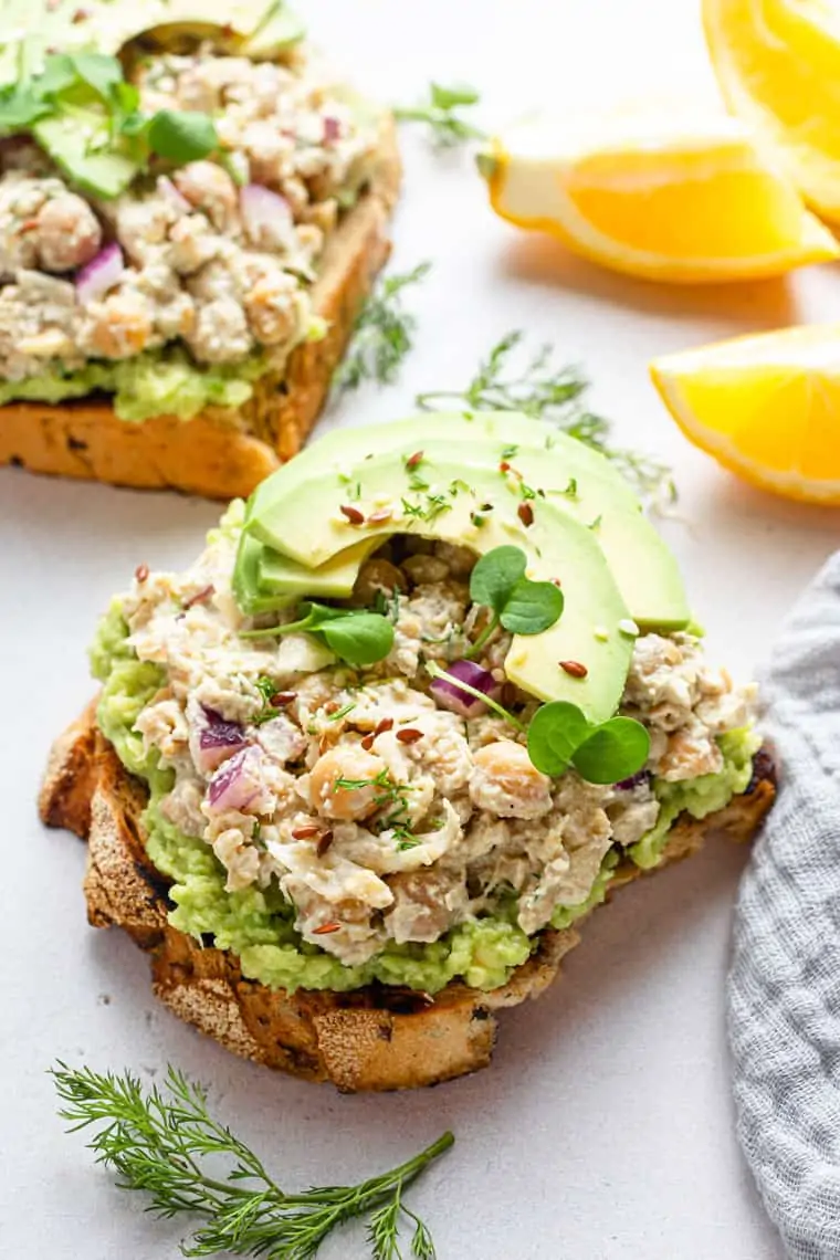 two slices of bread with smashed chickpea caesar salad and avocado