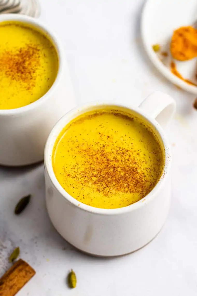 overhead of two white mugs with golden milk latte dusted with cinnamon on top