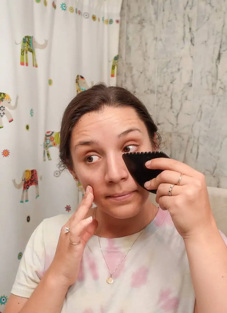woman using black gua sha tool under eye