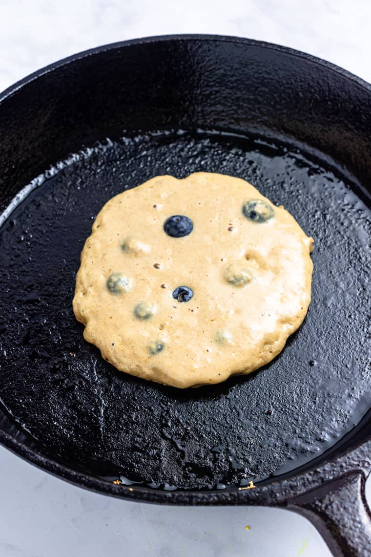 skillet with a single blueberry pancake cooking