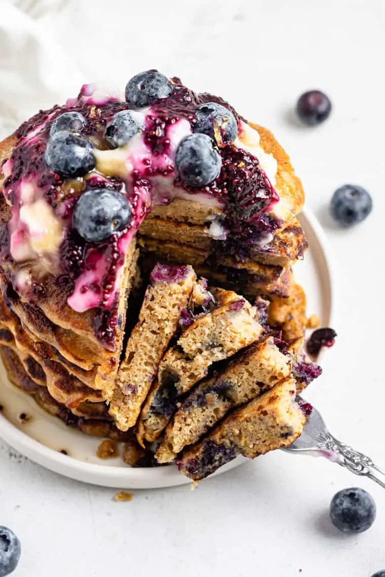 white plate with a stack of vegan blueberry pancakes topped with fresh berries and blueberry sauce