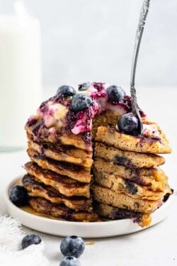stack of lemon blueberry pancakes with a bite cut out and a fork stuck in with blueberries and sauce