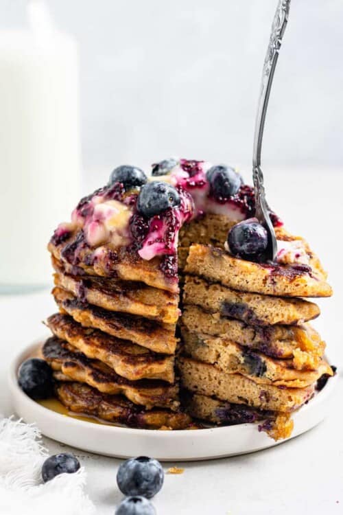 stack of vegan blueberry pancakes with a bite cut out and a fork stuck in with blueberries and sauce