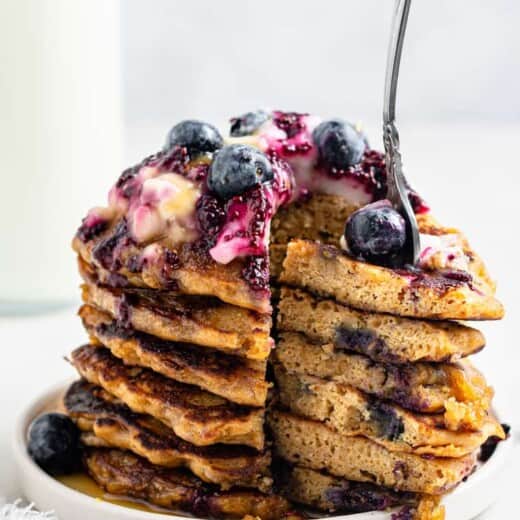 stack of lemon blueberry pancakes with a bite cut out and a fork stuck in with blueberries and sauce