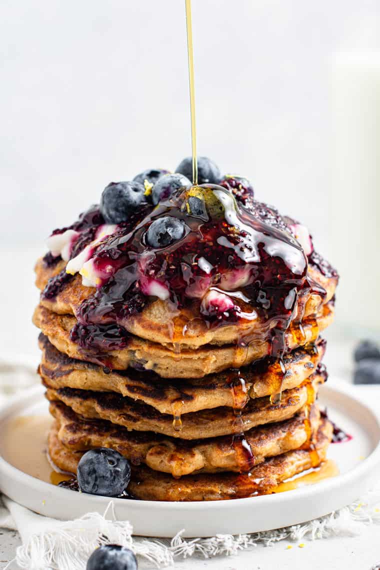 whole stack of vegan lemon blueberry pancakes with a drizzle of maple syrup poured on top
