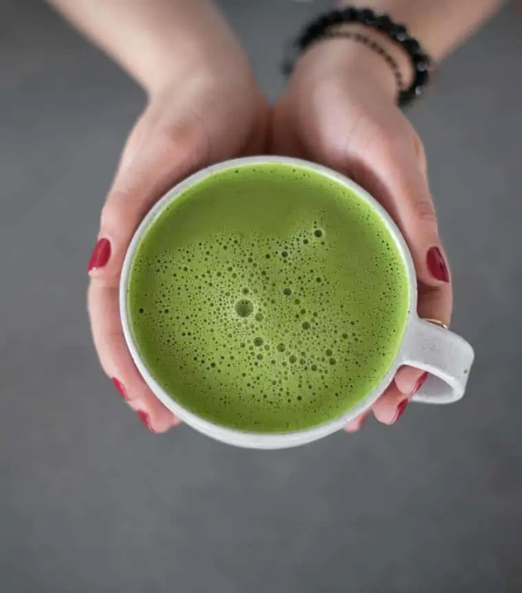 overhead of two hands holding a white mug with a matcha green tea latte inside