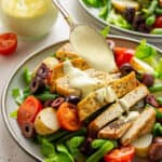 close up on a spoon drizzling dressing on top of sliced tofu with salad under