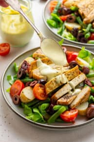 close up on a spoon drizzling dressing on top of sliced tofu with salad under