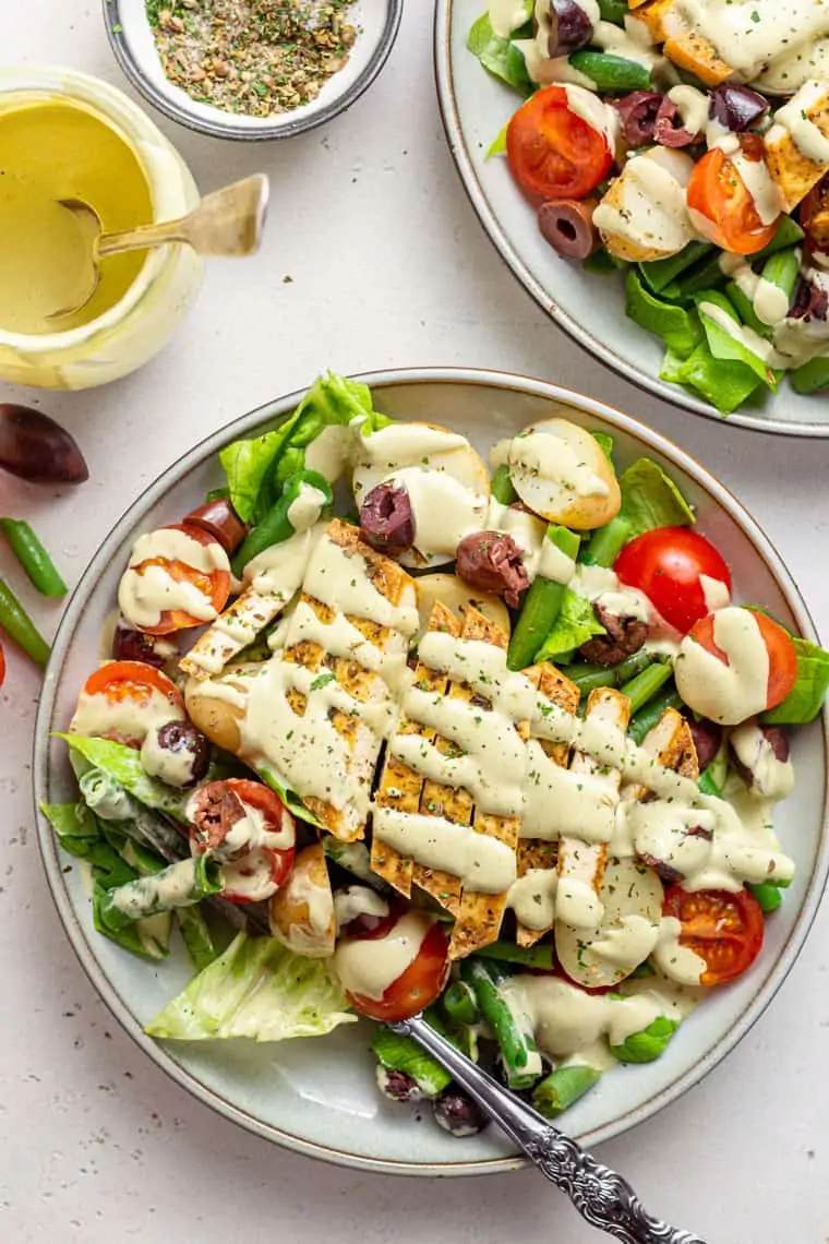 overhead of two plates with nicoise salad topped with sliced tofu and creamy dressing