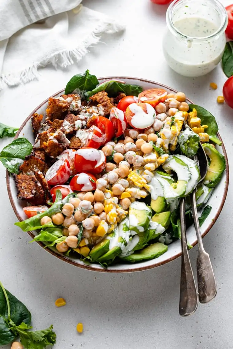 overhead of a large serving bowl with vegan cobb salad tomatoes, chickpeas and tempeh bacon with creamy dressing