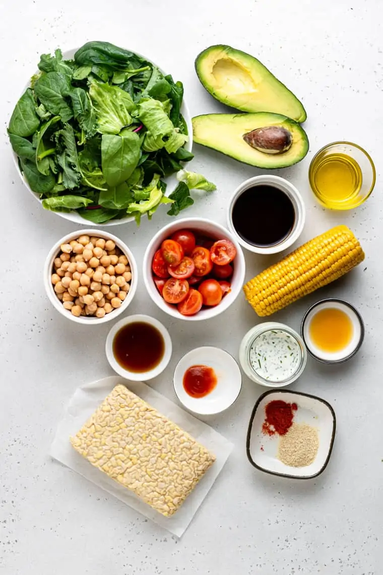 overhead of ingredients for vegan cobb salad with vegetables, corn, tempeh bacon and avocado