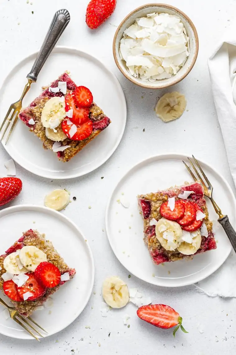 three plates with squares of baked oatmeal topped with strawberries and coconut