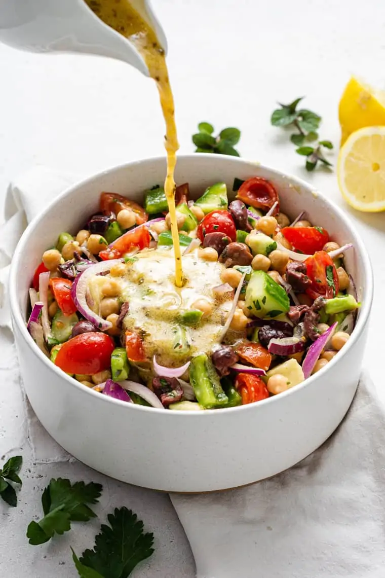 pouring dressing over chickpea and vegetable salad in a white bowl