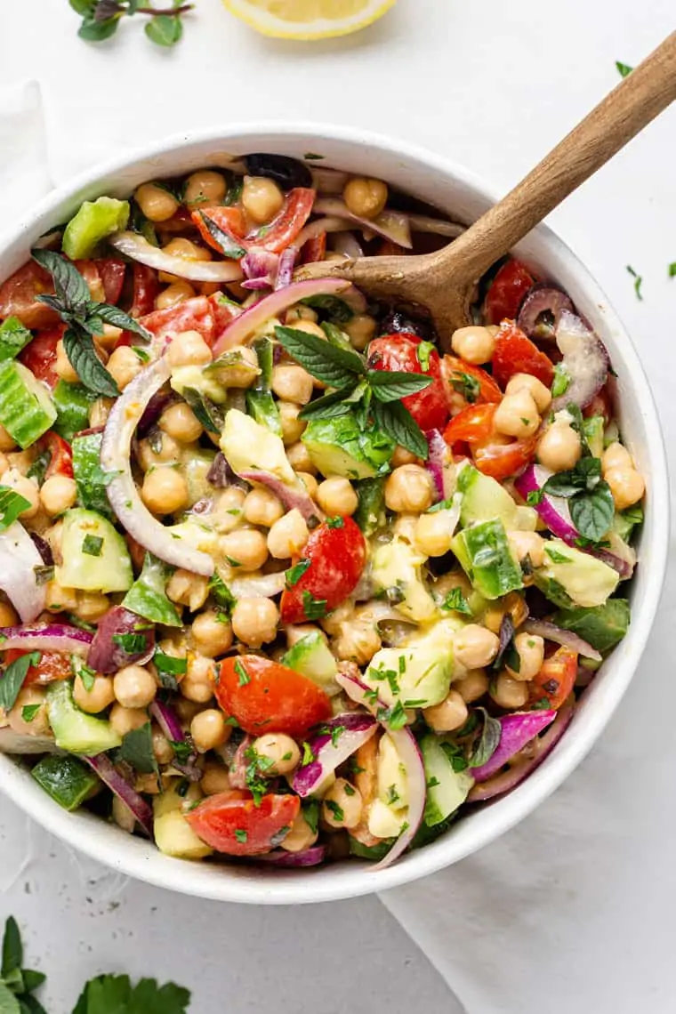 overhead of a large white bowl with colorful chickpea salad and dressing